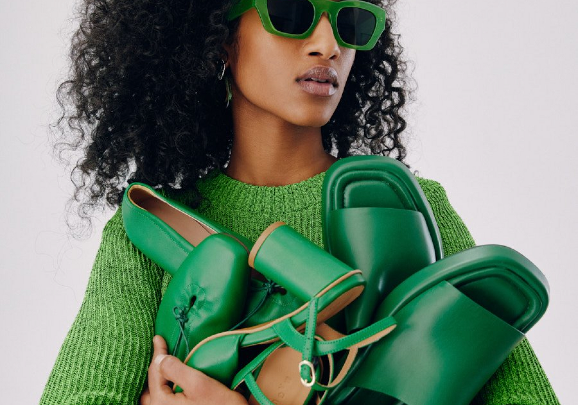 A woman dressed in green holding a few matching green shoes.