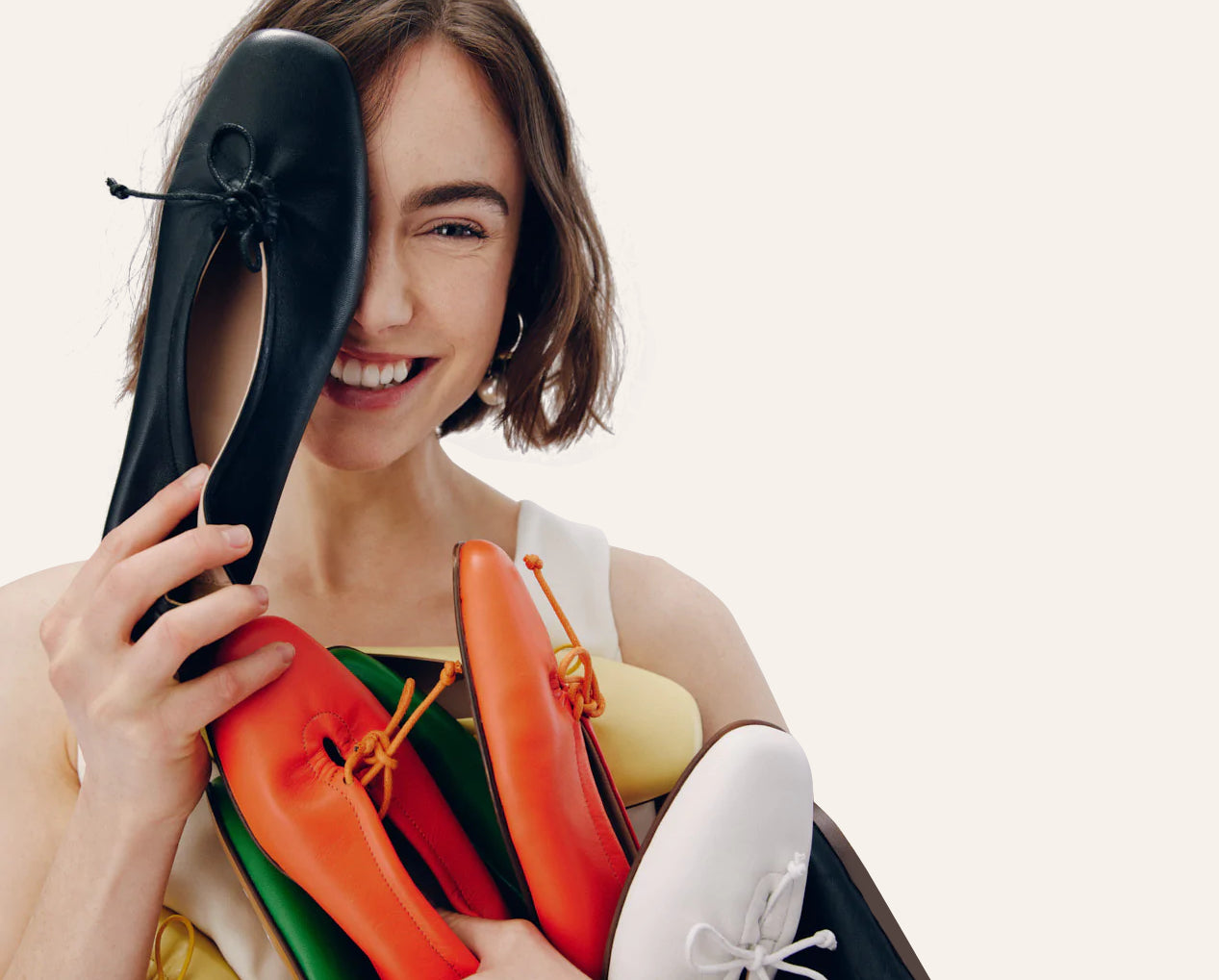 A smiling woman holding many pairs of shoes of different colors.